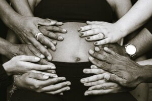 many hands on a pregnant abdomen